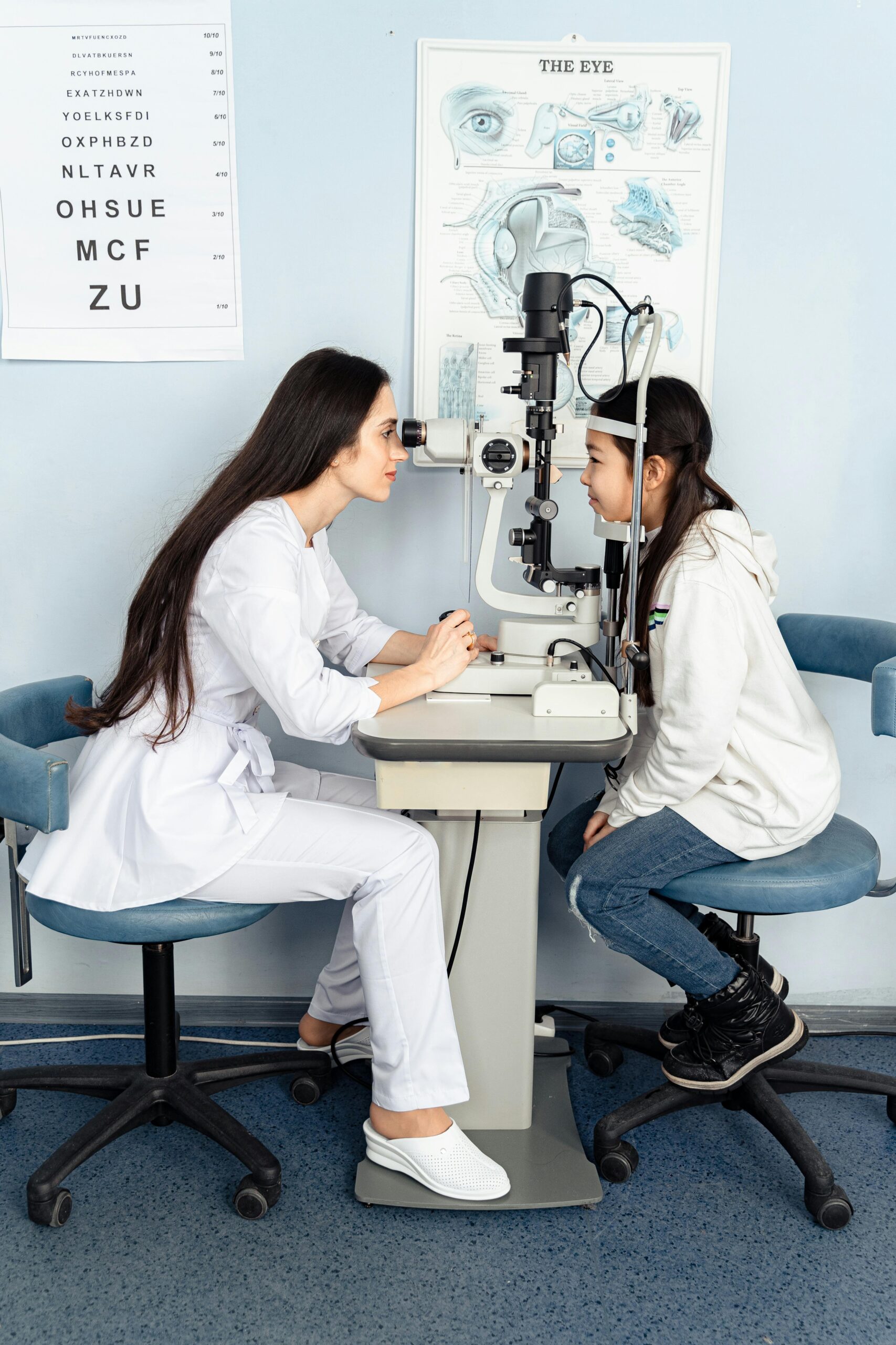 An optometrist performing an eye examination on a young girl in a clinic setting.